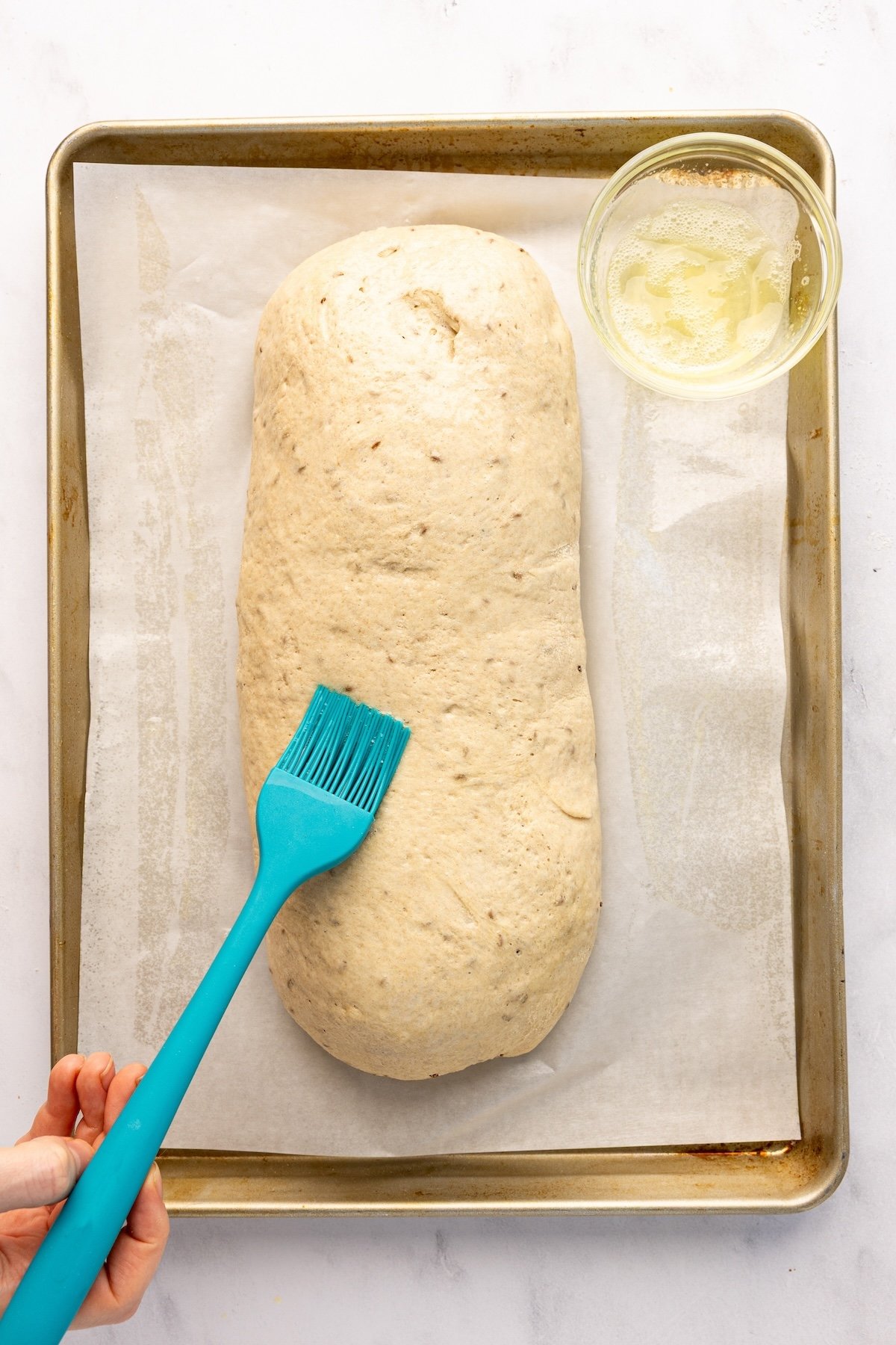 brushing egg white mixture onto risen dough loaf