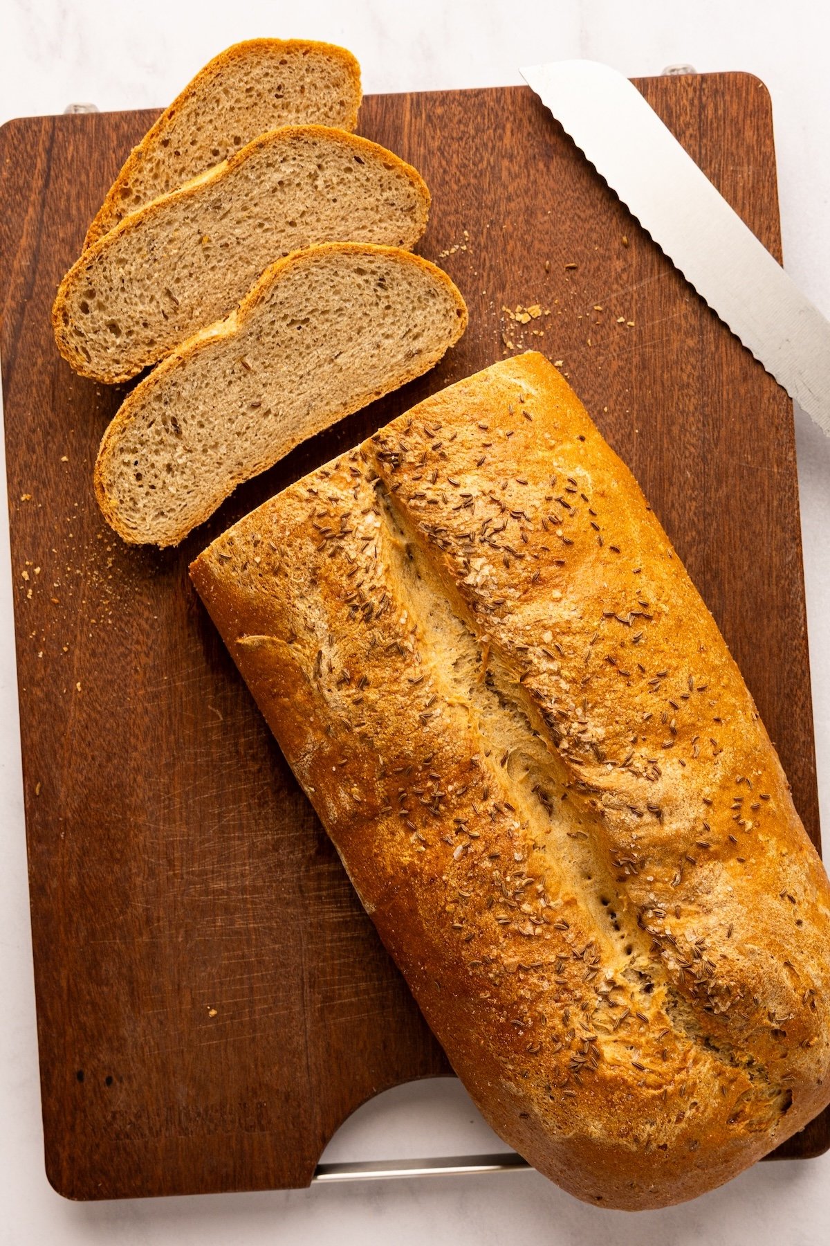 wooden cutting board with partially sliced rye bread loaf