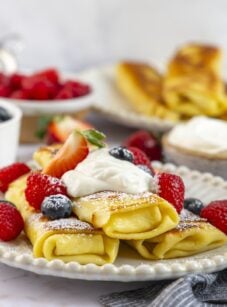 Cheese blintzes stacked on plate with sour cream and berries