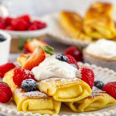 Blintzes au fromage empilés sur une assiette avec de la crème sure et des baies