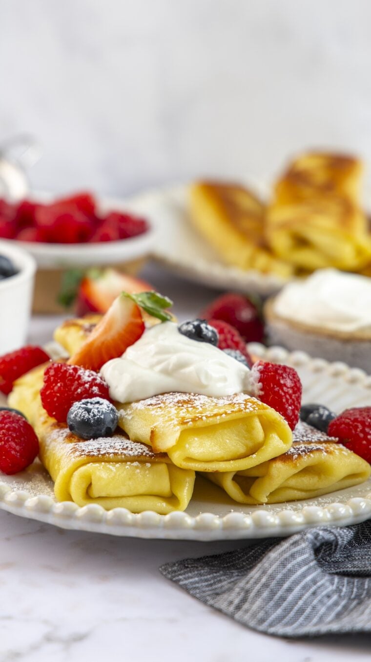 Blintzes au fromage empilés sur une assiette avec de la crème sure et des baies