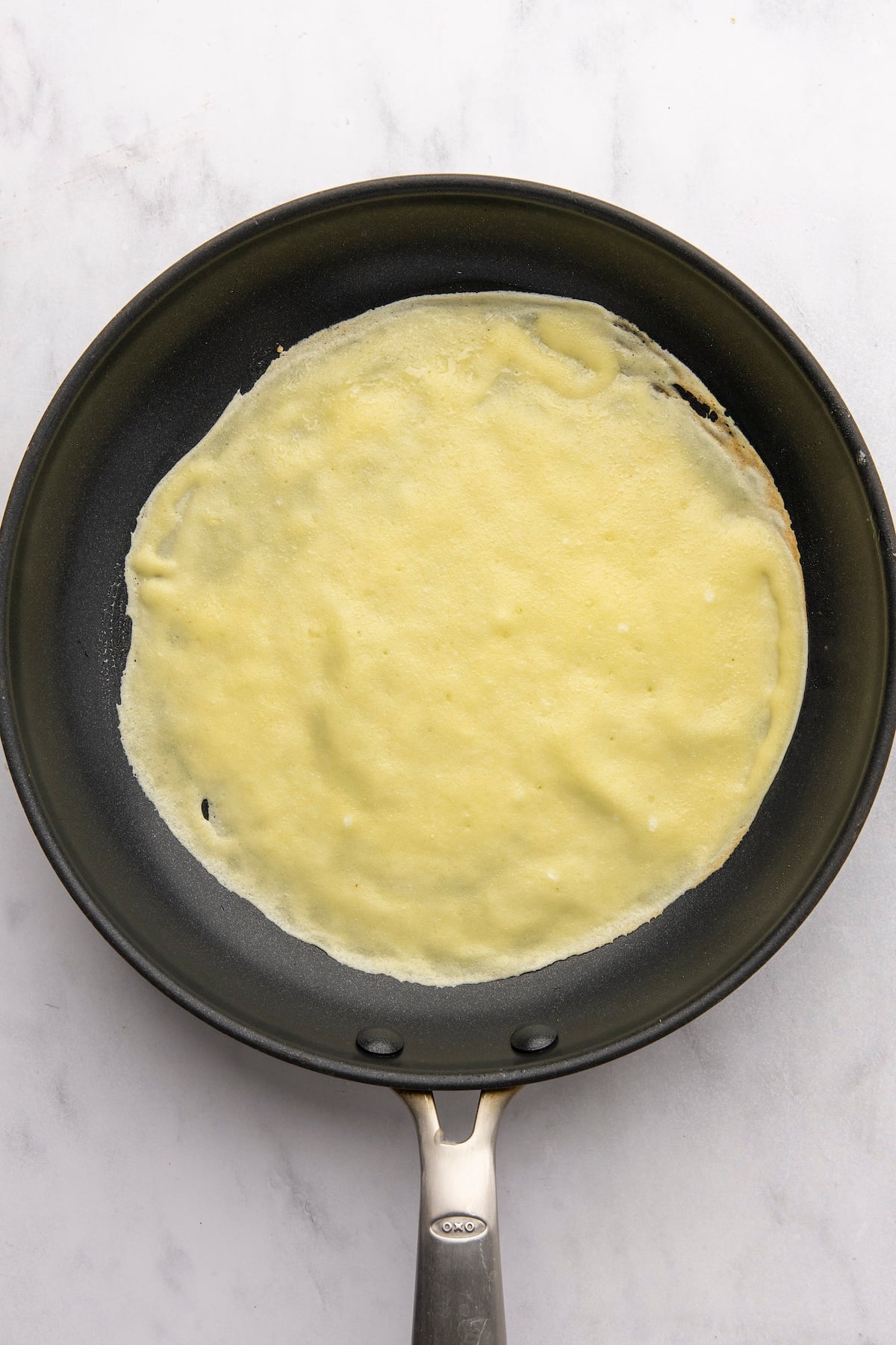 first side of crepe cooking in nonstick pan