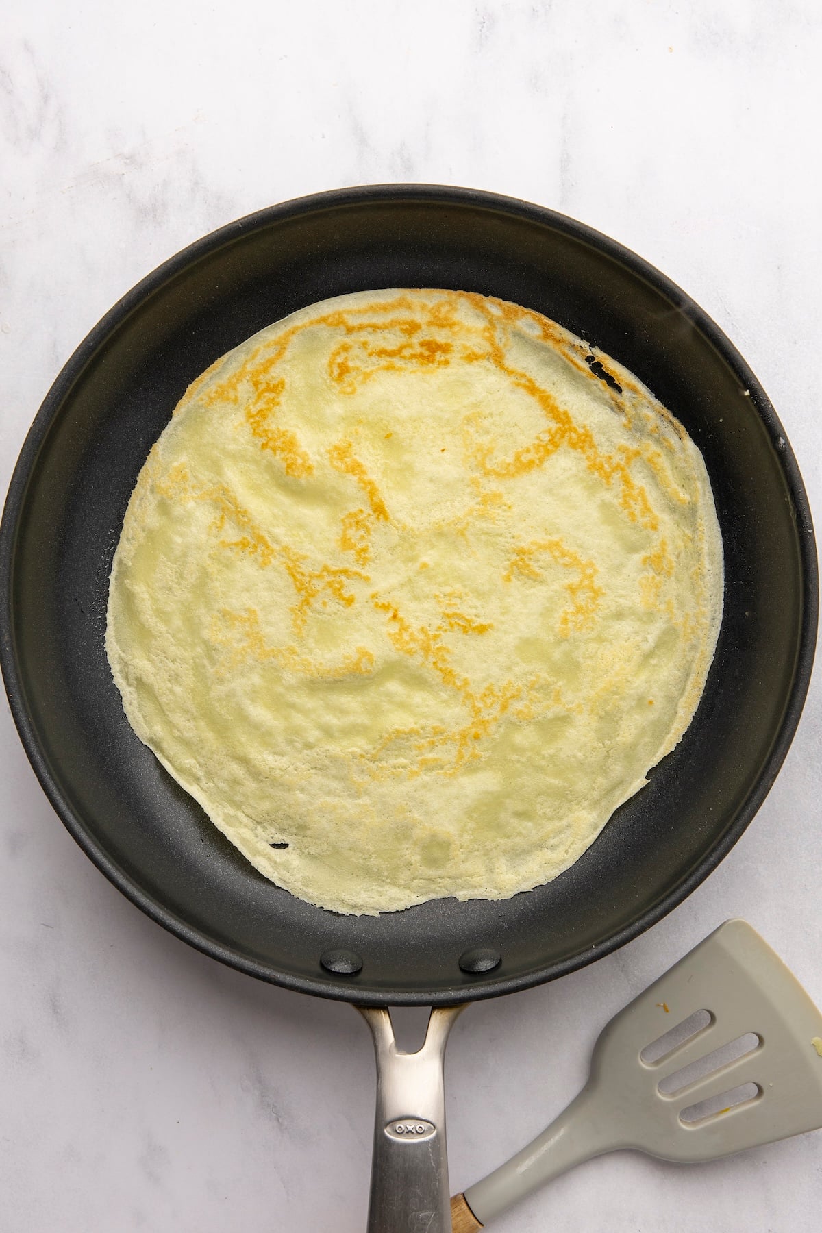 second side of crepe cooking in nonstick pan