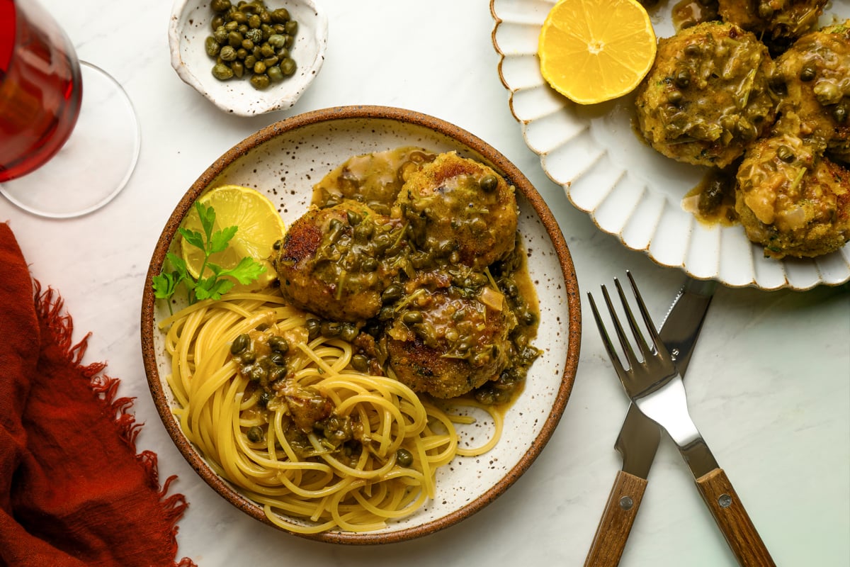 Chicken piccata meatballs with pasta and a glass of red wine.