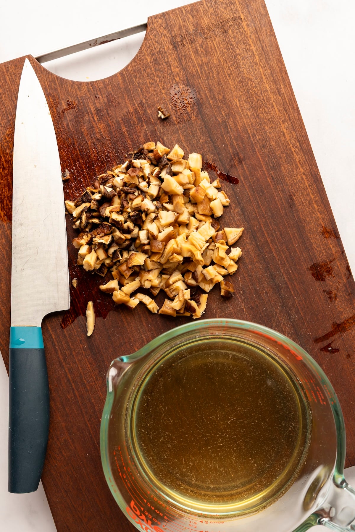 cutting board with chopped rehydrated mushrooms and measuring cup with soaking liquid