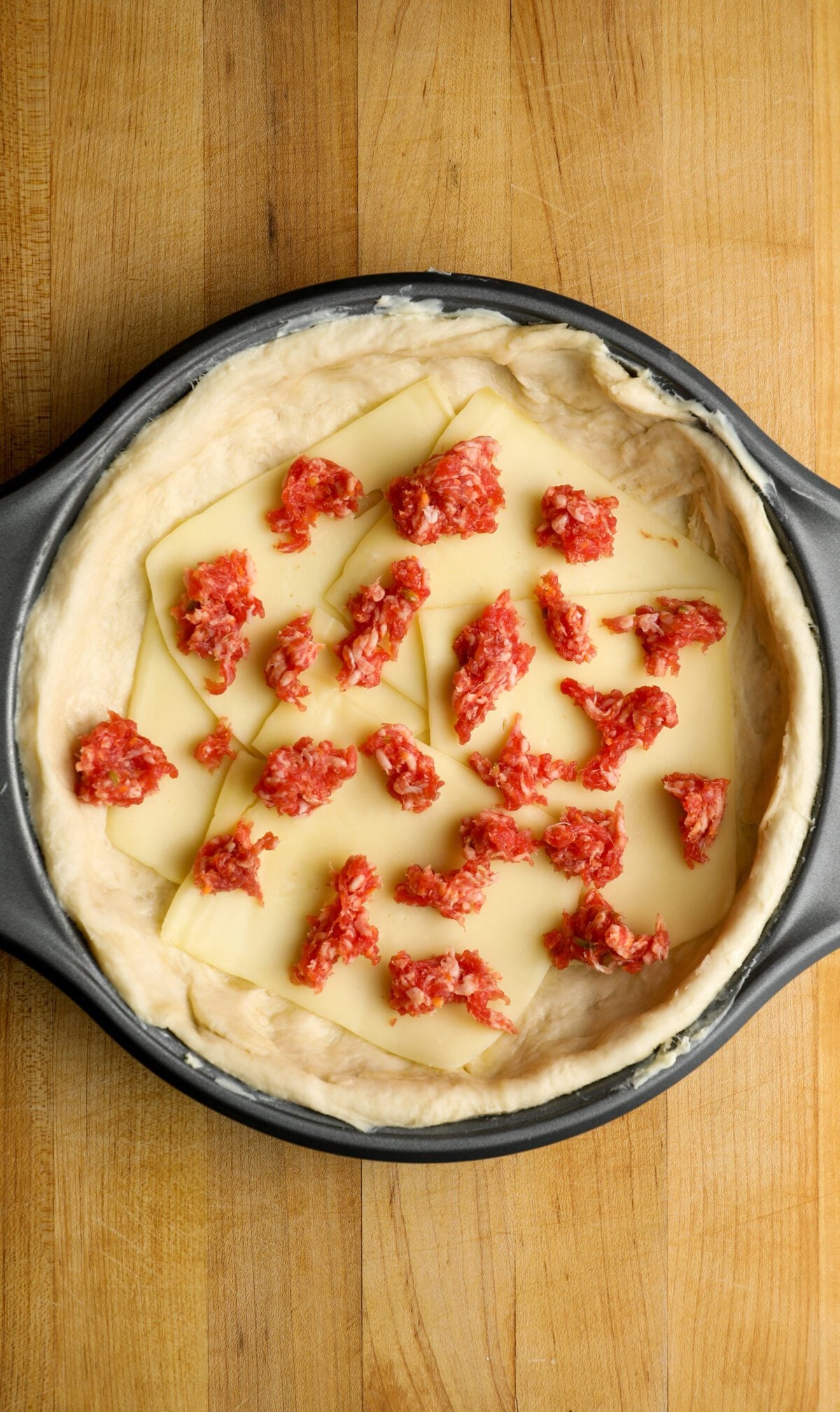 pizza dough in 9-inch baking pan topped with sliced mozzarella and sausage pieces