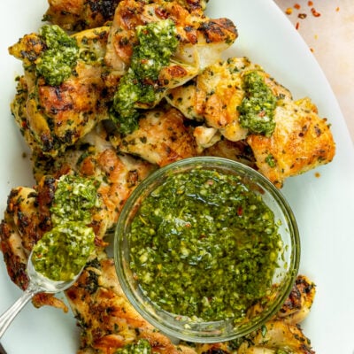 Grilled chimichurri chicken thighs on platter with chimichurri sauce.