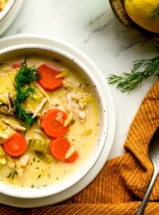two bowls of lemon chicken orzo soup with orange linen napkin and fresh dill