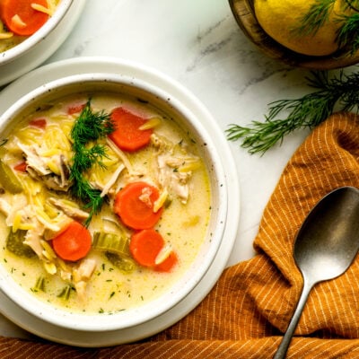 two bowls of lemon chicken orzo soup with orange linen napkin and fresh dill