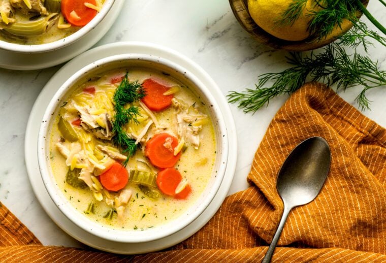 two bowls of lemon chicken orzo soup with orange linen napkin and fresh dill