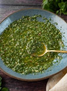 Fresh chimichurri sauce in blue bowl on wood table.