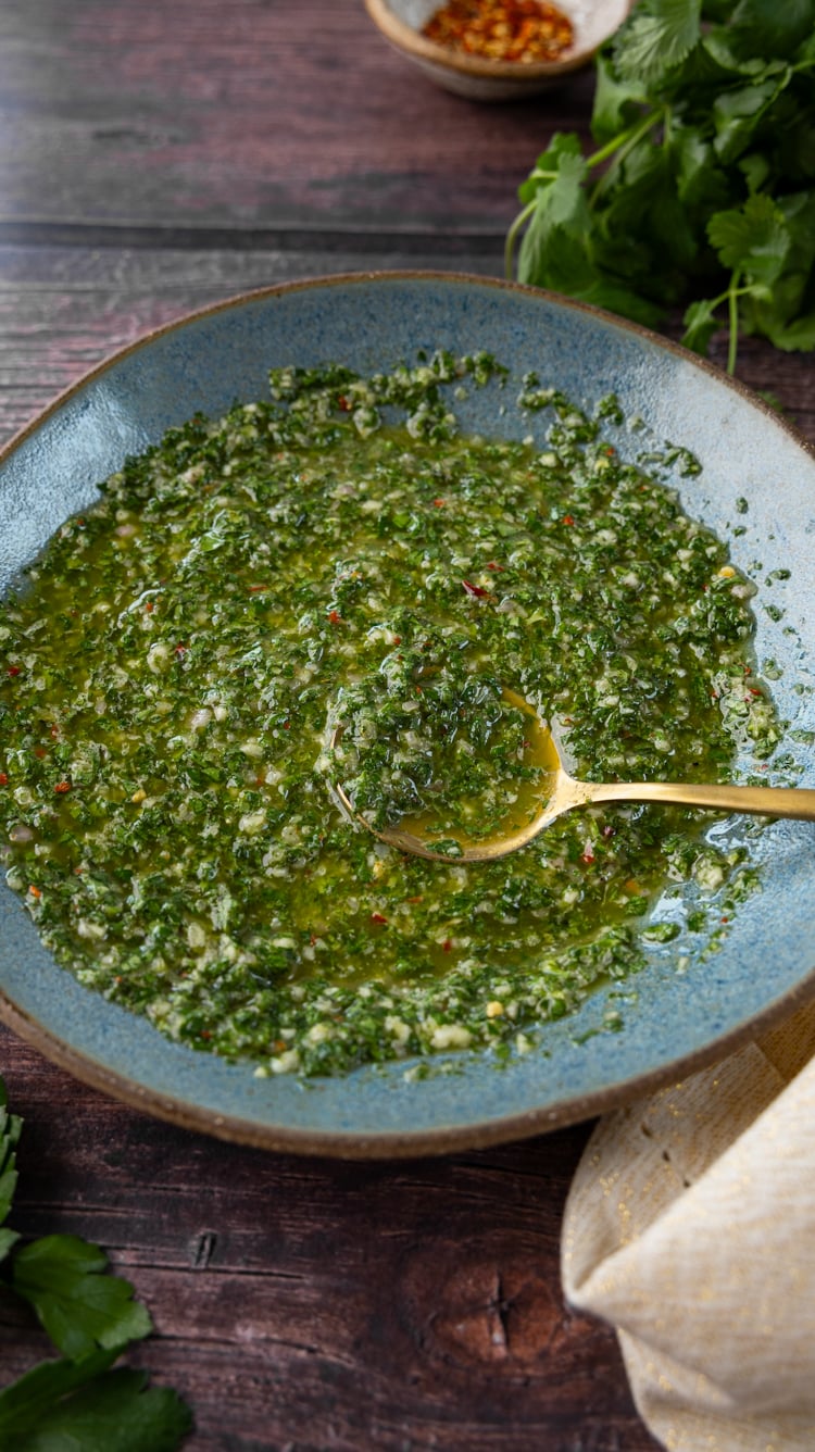 Fresh chimichurri sauce in blue bowl on wood table.