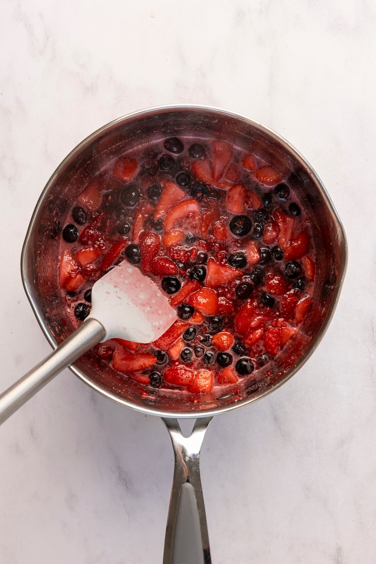 medium saucepan with spatula stirring berry/sugar mixture 