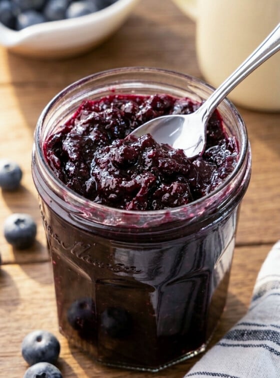 Jar of blueberry jam with spoon and striped napkin.