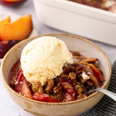 Plum crisp in a bowl with vanilla ice cream.
