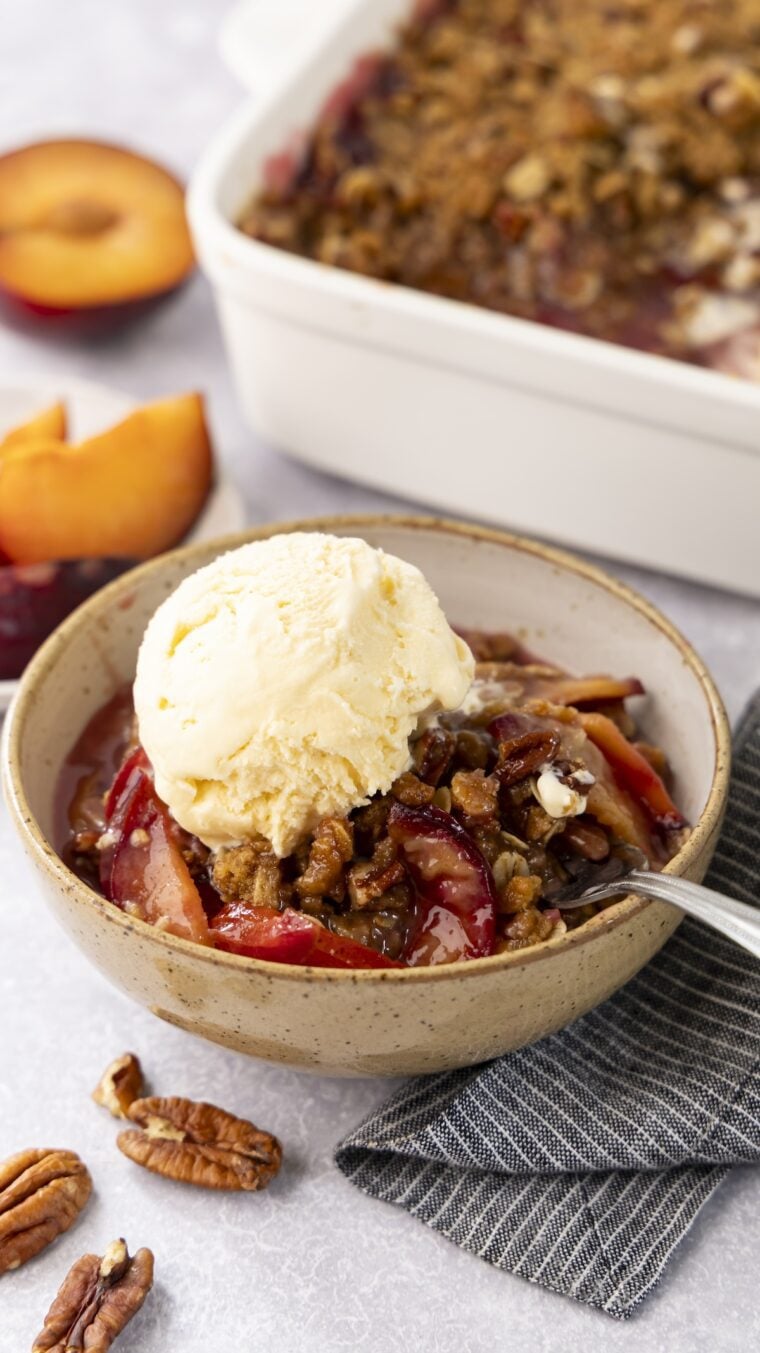 Plum crisp in a bowl with vanilla ice cream.