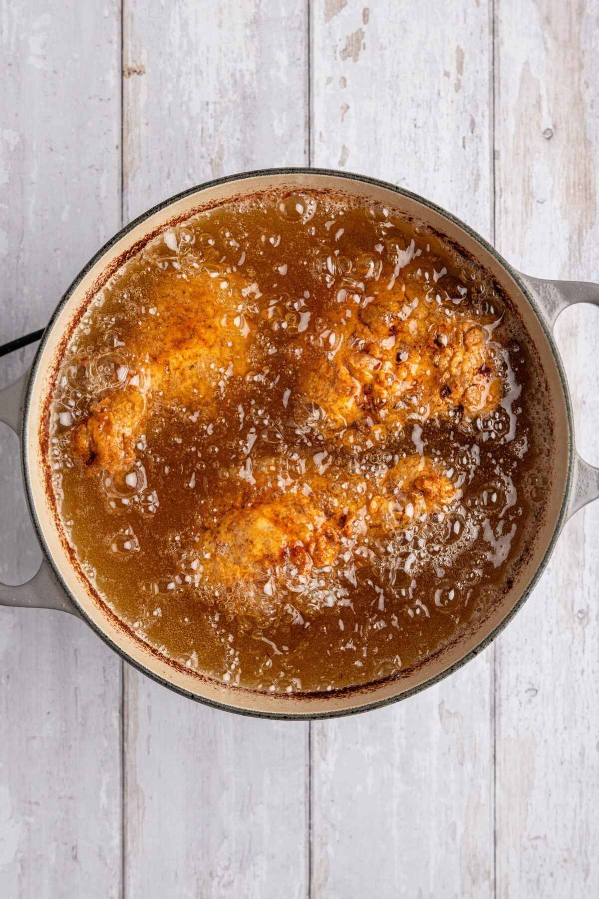 large dutch oven with browned chicken pieces in bubbling oil