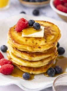 white plate with stack of cottage cheese pancakes topped with maple syrup, butter, and berries