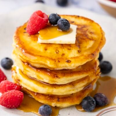 white plate with stack of cottage cheese pancakes topped with maple syrup, butter, and berries