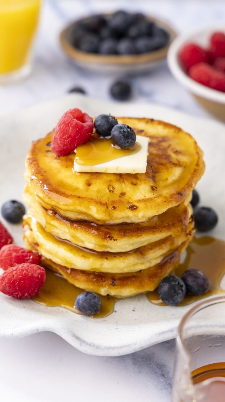 white plate with stack of cottage cheese pancakes topped with maple syrup, butter, and berries