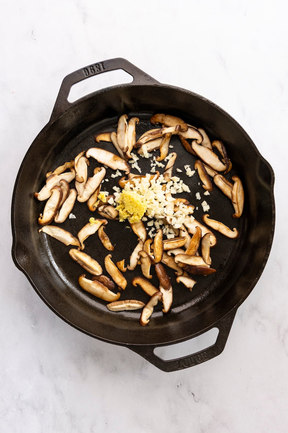 Adding garlic and ginger to cooked mushrooms in skillet.