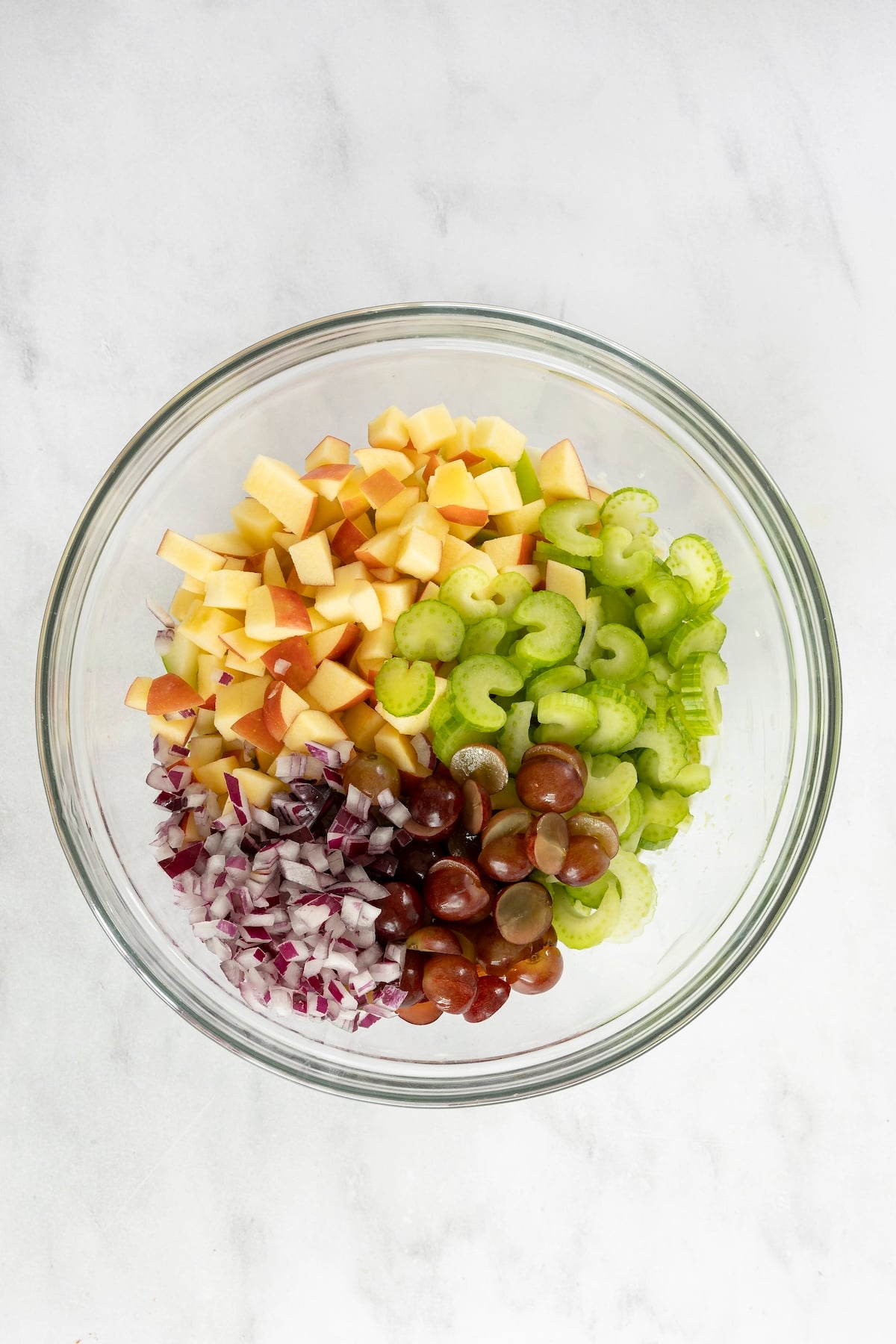 Large bowl with apples, celery, grapes, and red onion added to dressing