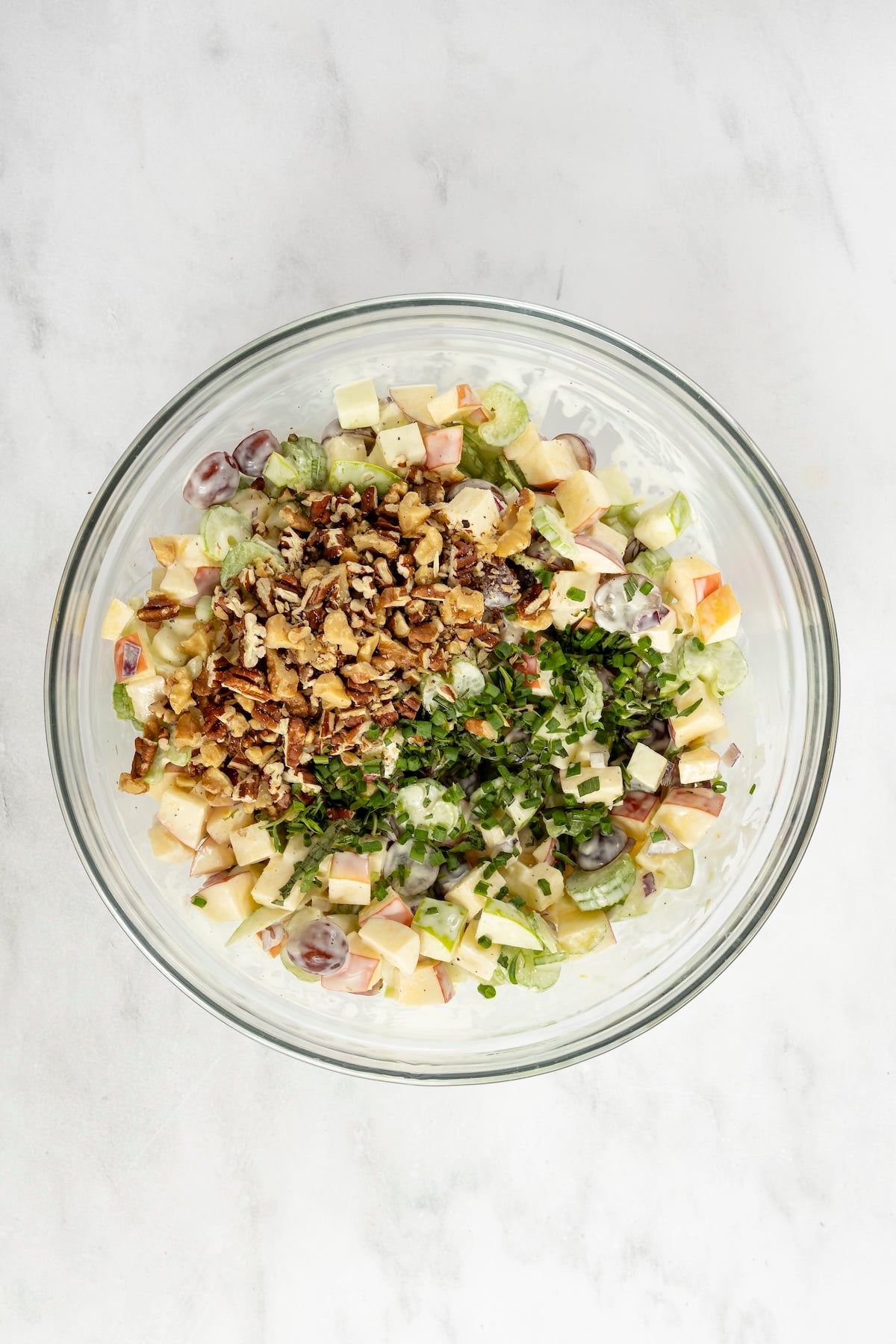 large bowl with nuts and herbs added to waldorf salad