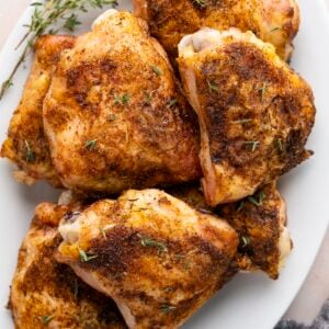 baked chicken thighs on white oval platter garnished with fresh thyme