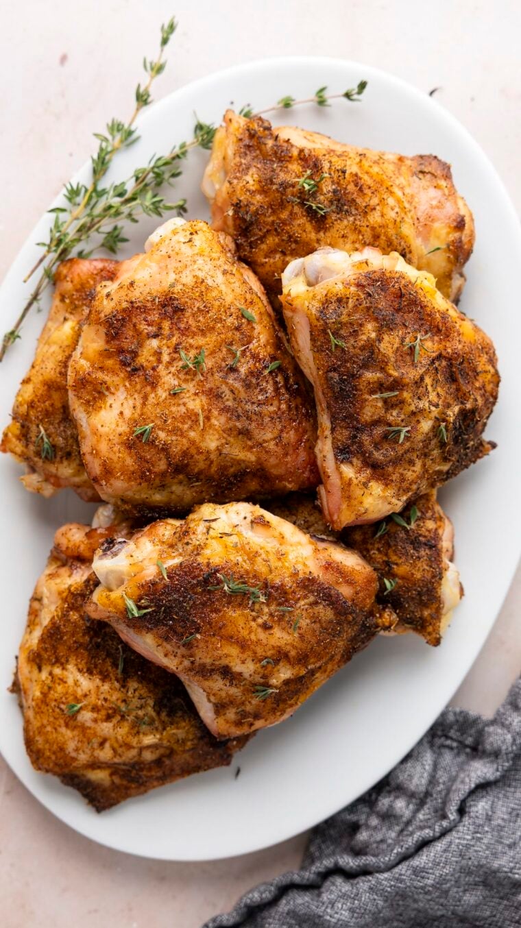 baked chicken thighs on white oval platter garnished with fresh thyme