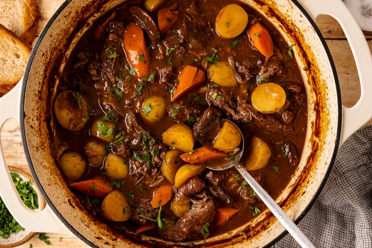 Hearty beef stew with vegetables on wood table.