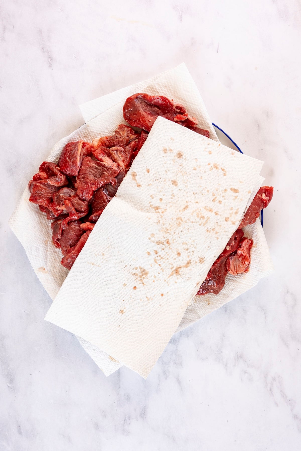 Patting chunks of beef dry with paper towels.