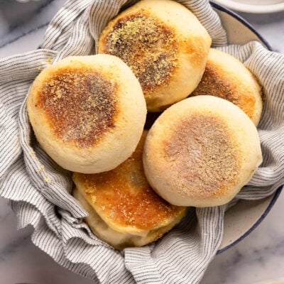 Whole english muffins in bowl with toasted English muffins on plates.