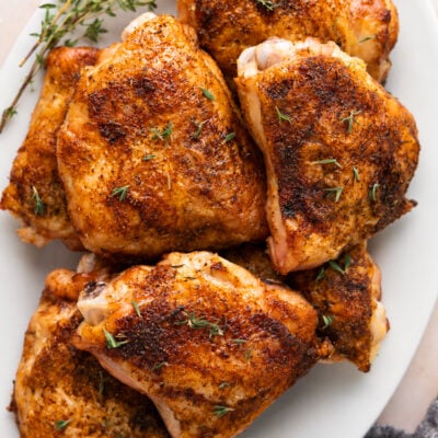 baked chicken thighs on white oval platter garnished with fresh thyme