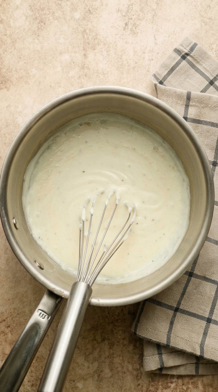 Bechamel sauce in pot with whisk.