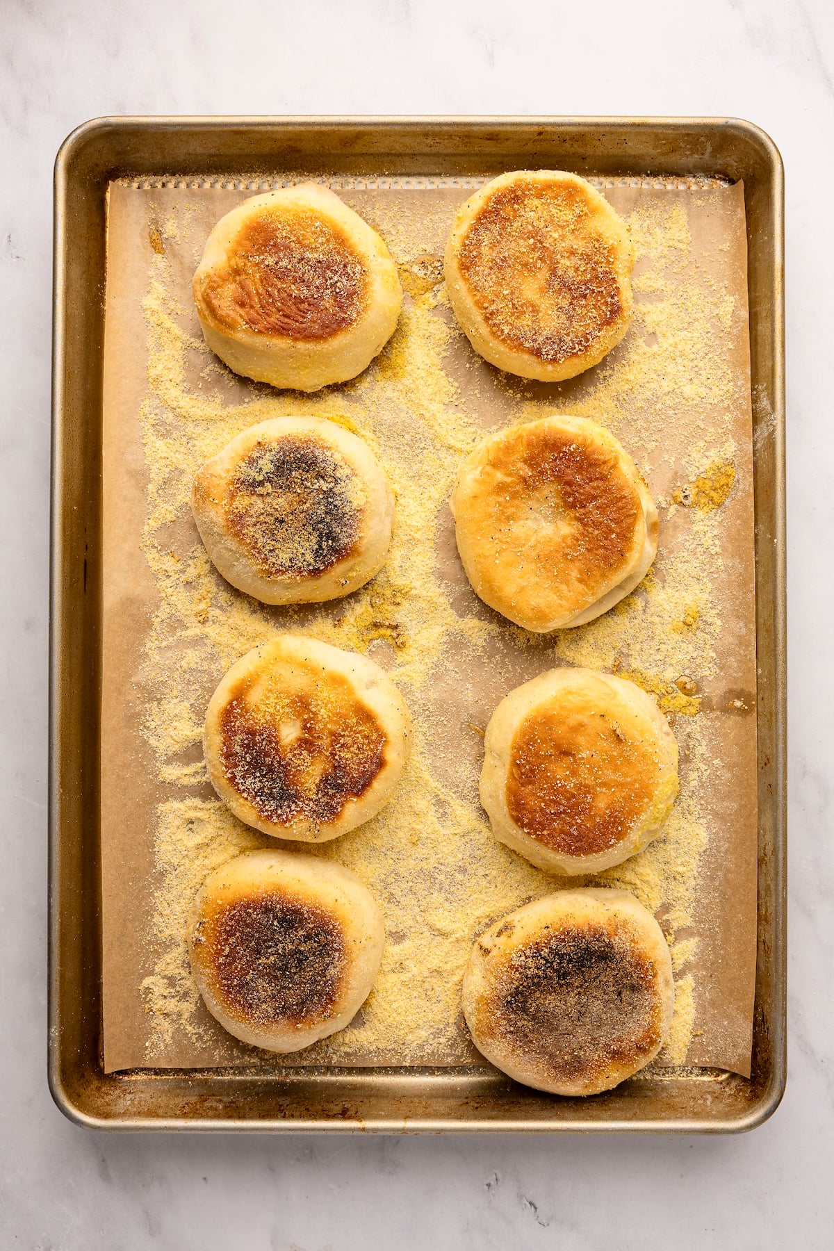 Parchment-lined baking sheet with baked English muffins